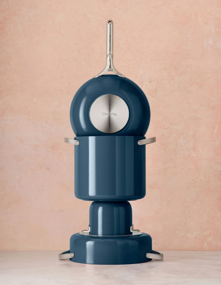 Image of a caraway cookware set with a stock pot in a navy blue stacked artistically against a peach background. 